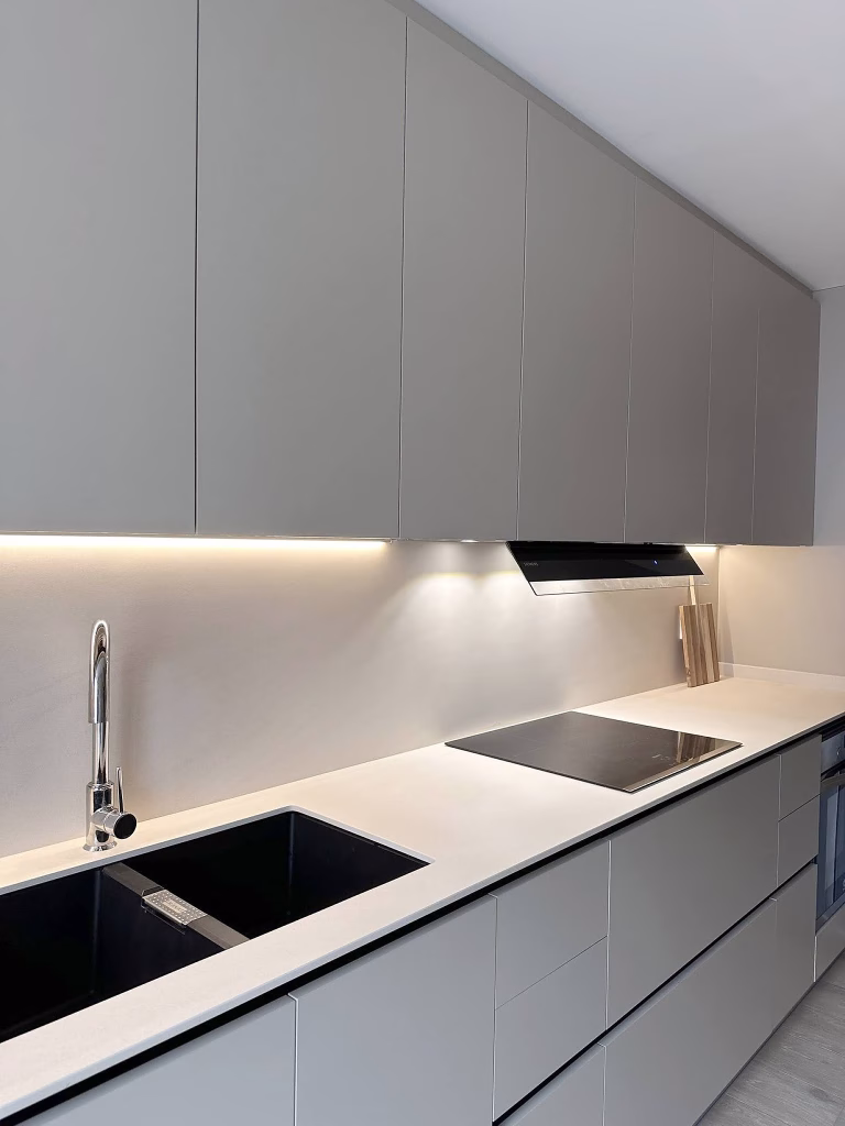 Cocina moderna en tonos grises con encimera clara e iluminación LED.