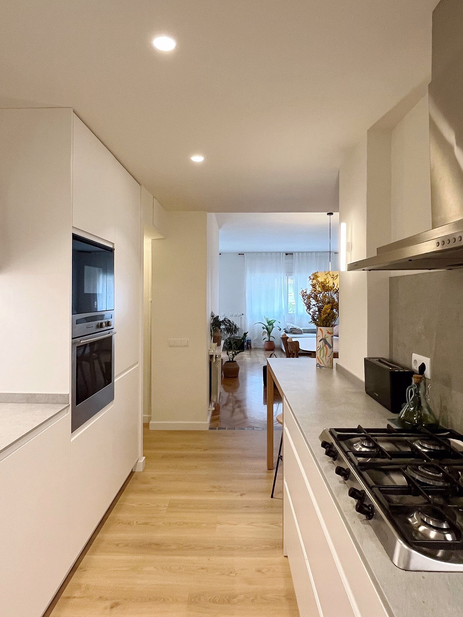 Cocina alargada en blanco con encimera clara y salida al salón